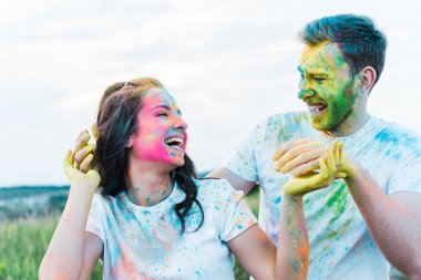 mutlu genç kadın yüzünde holi boyalar ile adam yakınında gesturing sırasında gülümseyen 