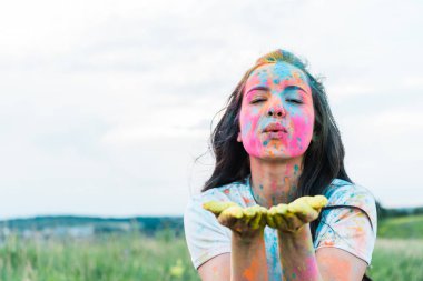 renkli holi boyalar ile çekici genç kadın kameraya bakarak ve hava öpücük gönderme yüzünde