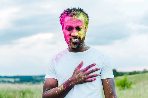 happy african american man in white t-shirt and colorful holi paints on face