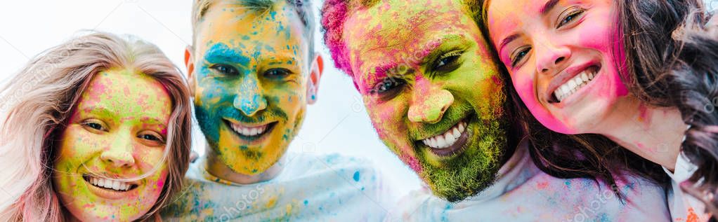 panoramic shot of happy multicultural friends with colorful holi paints on faces