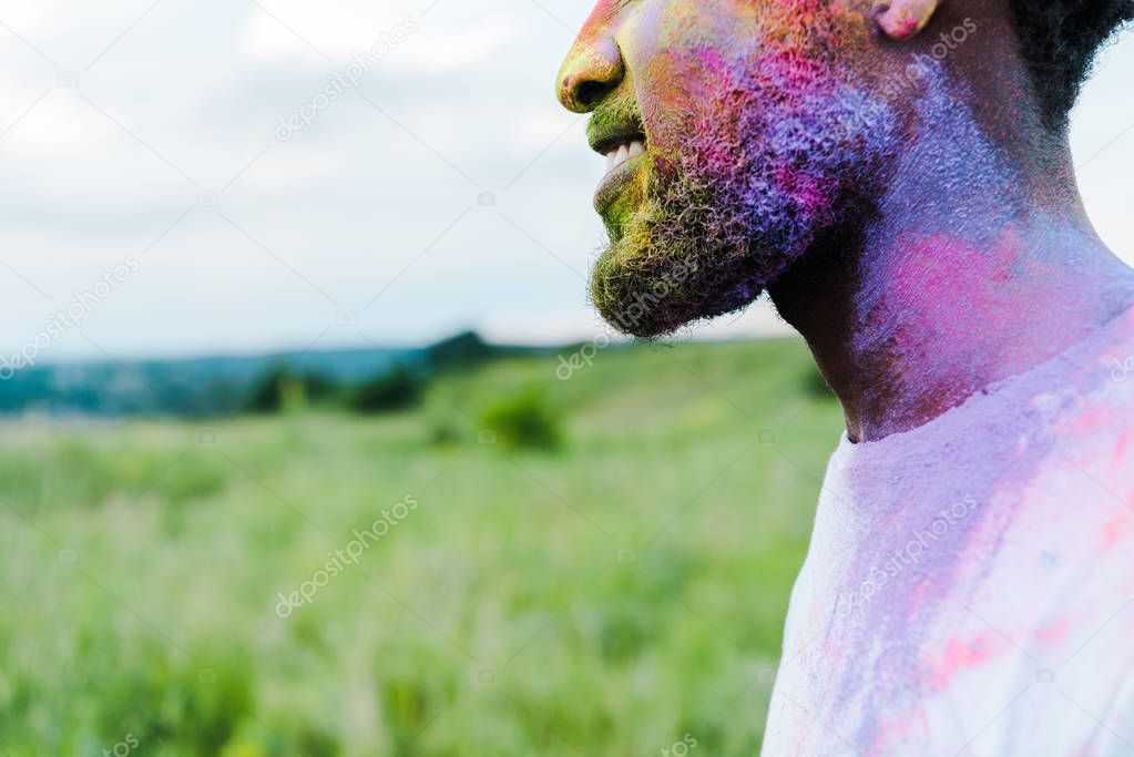 cropped view of cheerful african american man with colorful holi paints on face 
