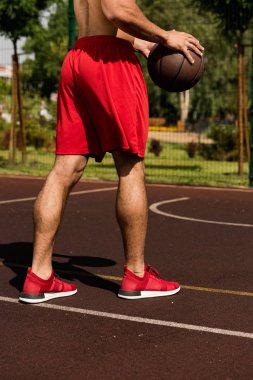 partial view of basketball player with ball at basketball court in sunny day clipart