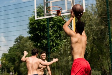 güneşli bir günde basketbol sahasında basketbol oynayan gömleksiz sporcular