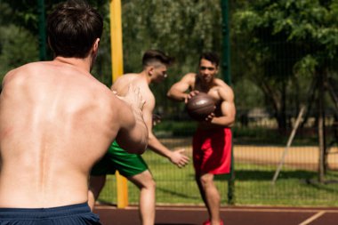 güneşli bir günde basketbol sahasında basketbol oynayan gömleksiz sporcular