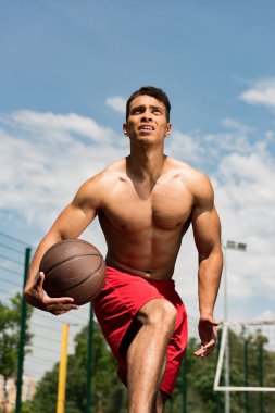mavi gökyüzü altında basketbol sahasında topu ile gömleksiz karışık yarış basketbol oyuncusu odaklı
