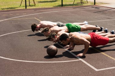 güneşli bir günde basketbol sahasında push up yapıyor dört seksi gömleksiz sporcular