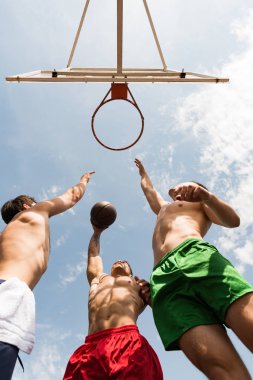 mavi gökyüzü altında basketbol oynayan gömleksiz sporcuların alt görünümü
