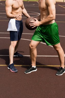 güneşli bir günde basketbol sahasında basketbol oynayan iki gömleksiz sporcuların kısmi görünümü