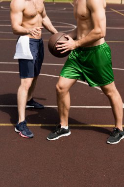 partial view of two shirtless sportsmen playing basketball at basketball court in sunny day clipart