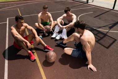 güneşli bir günde basketbol sahasında oturan dört yorgun gömleksiz basketbolcu