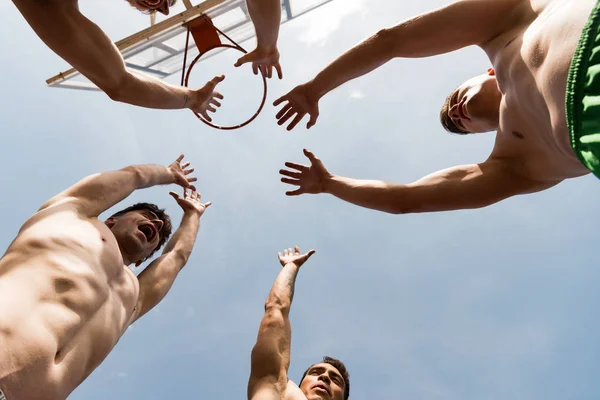 バスケットボールのバックボードの近くで空の下で手を上げる4人のシャツのないスポーツマンの下のビュー — ストック写真