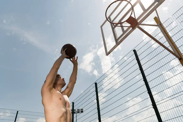 バスケットボールコートでバスケットにボールを投げるセクシーなシャツレスバスケットボール選手 — ストック写真