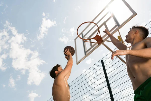 バスケットボールコートで青空の下でバスケットボールをしている2人のセクシーなシャツレススポーツマン — ストック写真