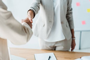 cropped view of recruiter and employee shaking hands while standing  in office  clipart