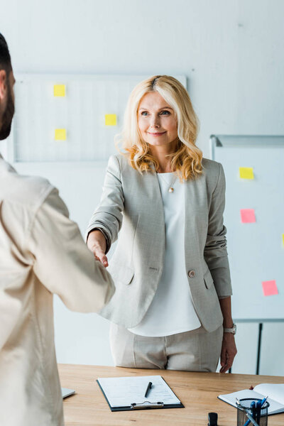 selective focus of blonde recruiter shaking hands with employee in office 