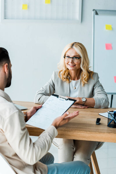 selective focus of woman in glasses looking at man holding clipboard in office 