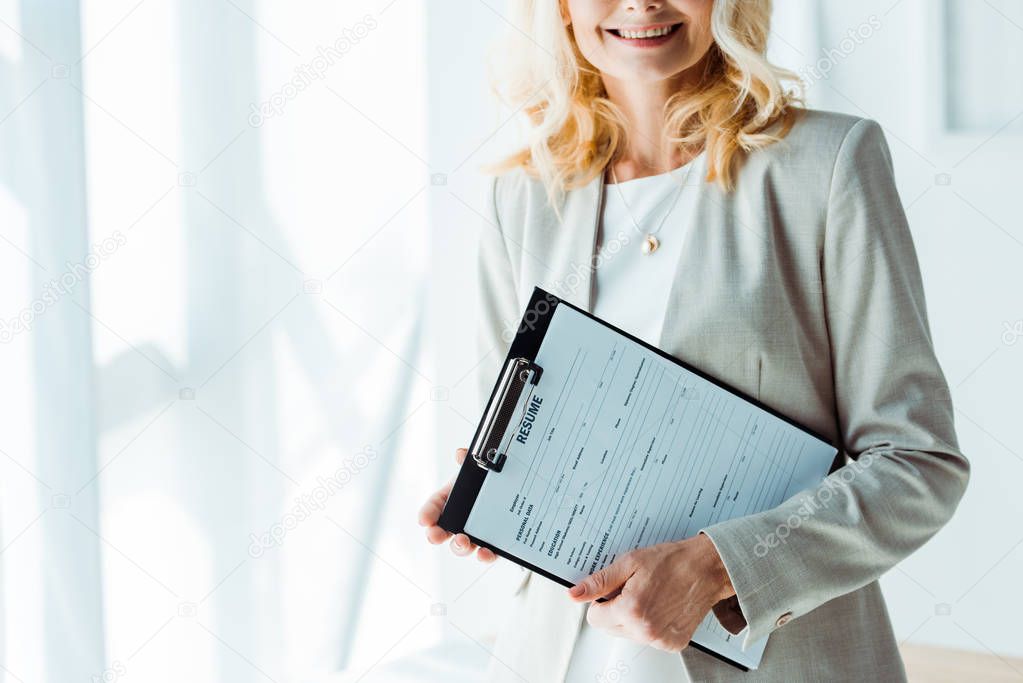 cropped view of cheerful blonde woman holding clipboard 