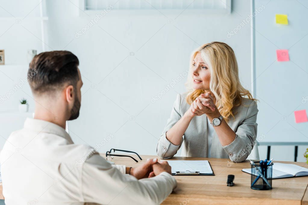 selective focus of blonde recruiter sitting with clenched hands bearded man 