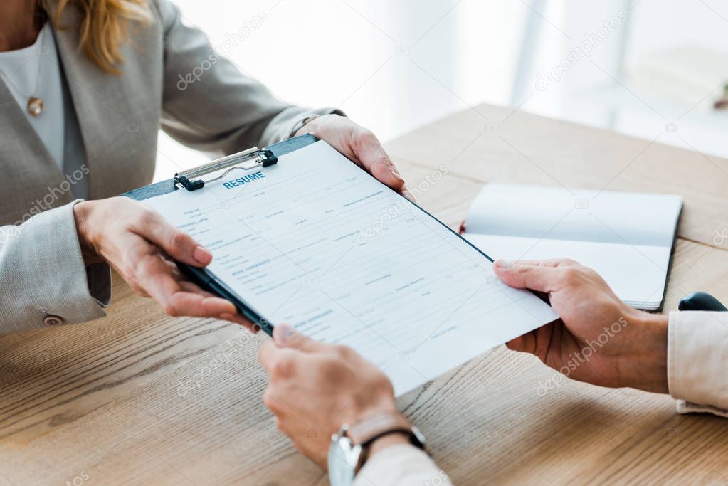 cropped view of recruiter giving clipboard with resume lettering to man 