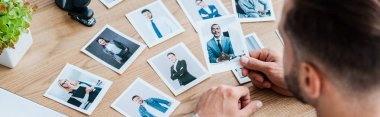 panoramic shot of recruiter choosing while holding photo near wooden table  clipart