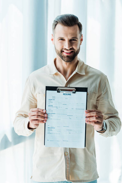cheerful bearded man holding clipboard with resume letters