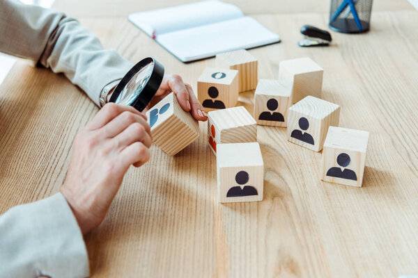 cropped view of recruiter holding magnifier near cube in office 