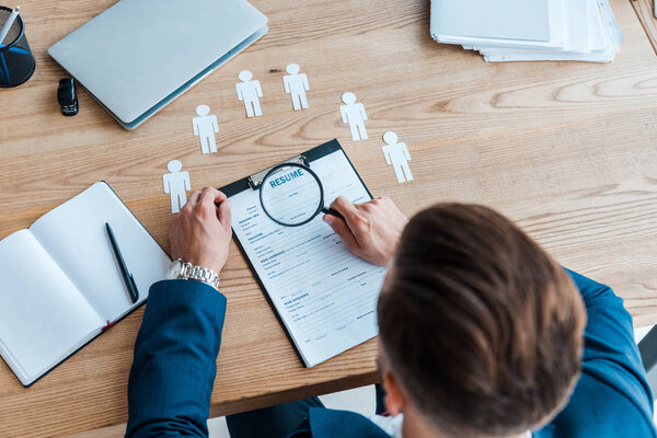 селективное фокусирование человека, держащего лупу возле буфера обмена с резюме
 