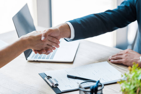 selective focus of employee and recruiter shaking hands near laptop 