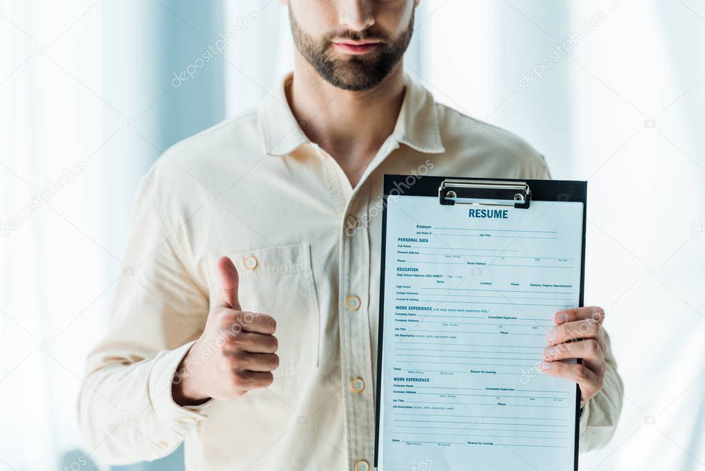 cropped view of bearded man showing thumb up and holding clipboard with resume letters 