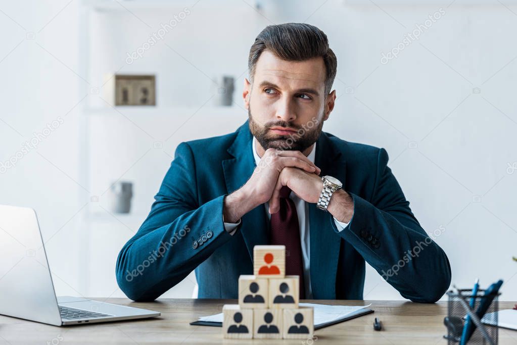 selective focus of pensive recruiter with clenched hands near wooden cubes 