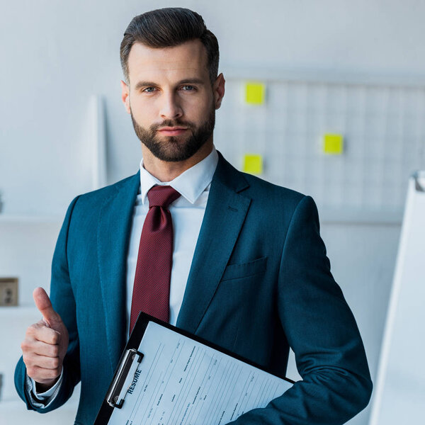 confident bearded man holding clipboard with resume letters and showing thumb up 