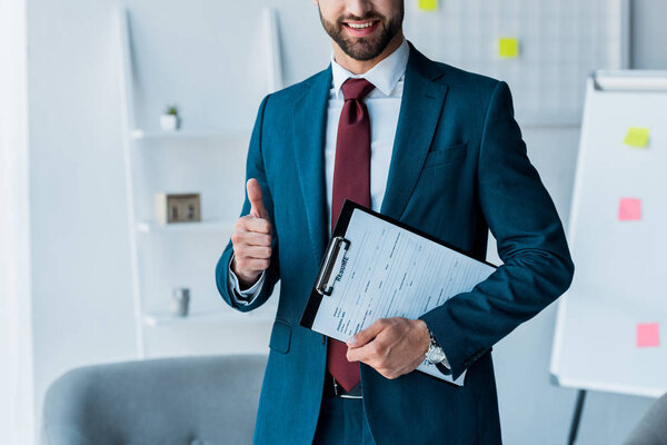cropped view of cheerful bearded man holding clipboard with resume letters and showing thumb up 