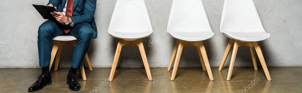 panoramic shot of man sitting on white chair and holding clipboard 