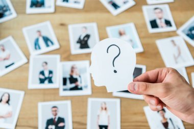 cropped view of man holding paper with human head and question mark near photos  clipart