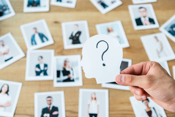 cropped view of man holding paper with human head and question mark near photos 