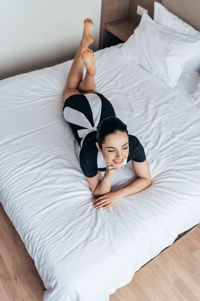ホテルの部屋でベッドに横たわっている裸足のメイドの笑顔のオーバーヘッドビュー — ストック写真