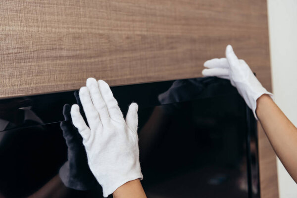 partial view of maid in white gloves touching tv iwith blank screen n hotel room