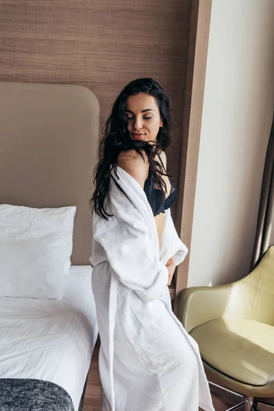性感的黑发年轻女子在内衣和白色浴袍与眼睛在卧室闭着眼睛 — 图库照片