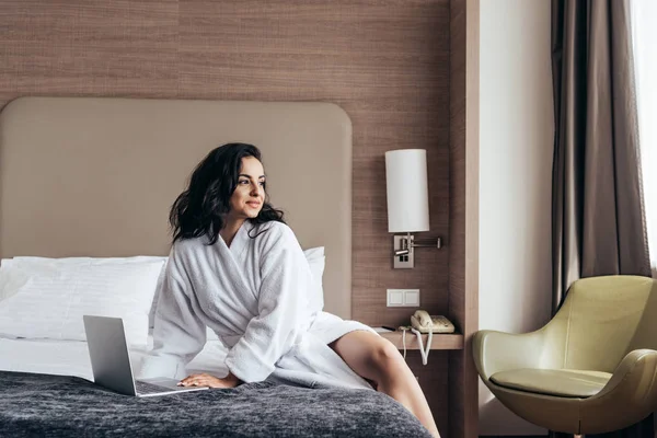 yatak odasında dizüstü bilgisayar kullanarak beyaz banyoda büyüleyici esmer genç kadın