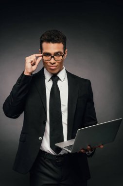 gözlük ve takım elbise yakışıklı afro-amerikan işadamı karanlık arka planda dizüstü bilgisayar tutan
