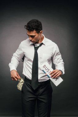 karanlık arka plan üzerinde iş gazetesi tutan cep nakit ile Afrikalı-Amerikalı işadamı
