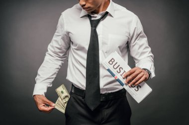 zengin afro-amerikan işadamı iş gazetesi tutan ve karanlık arka plan üzerinde cebinde banknotlar bakarak kırpılmış görünümü