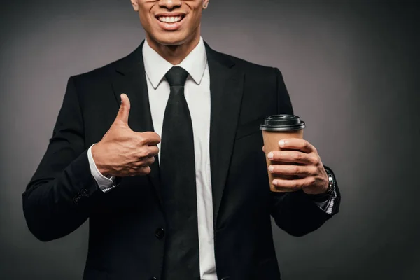 スーツを着たアフリカ系アメリカ人のビジネスマンがコーヒーを飲みながら 暗い背景に親指を立て続ける様子を見せた — ストック写真