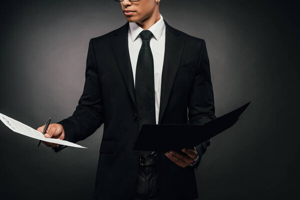 cropped view of african american businessman reading contract on dark background