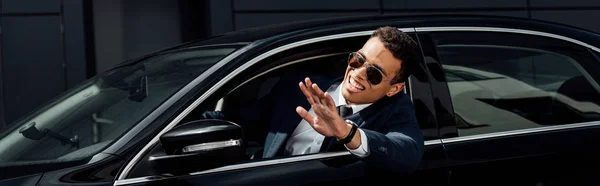 晴れた日に車から手を振るスーツとサングラスを着たアフリカ系アメリカ人ビジネスマン パノラマショット — ストック写真