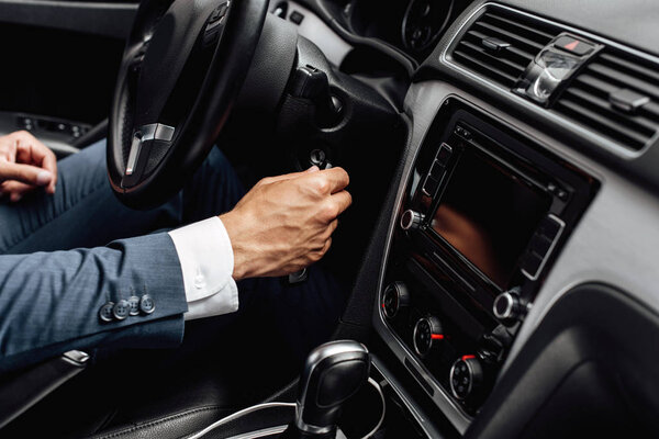 cropped view of african american businessman in suit starting car