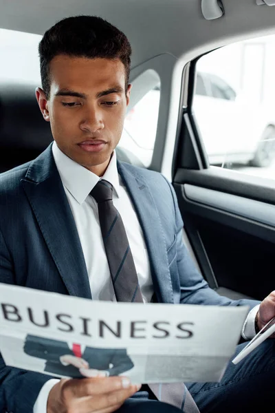 自信を持ってアフリカ系アメリカ人のビジネスマンが車の中でビジネス新聞を読む — ストック写真