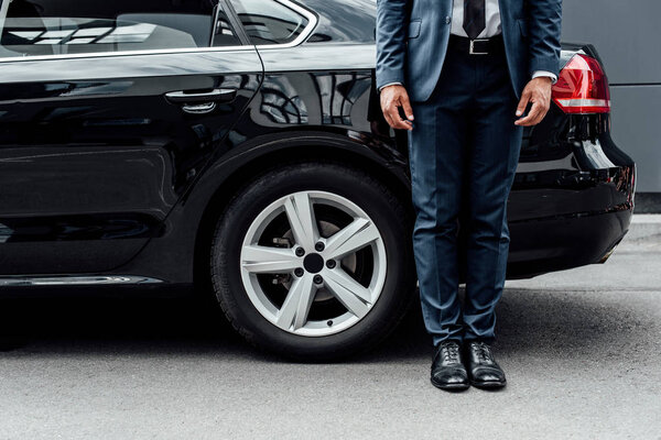 cropped view of african american man in suit standing near black car