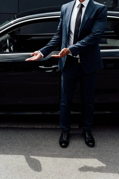 partial view of african american man in suit pointing with hands on car door