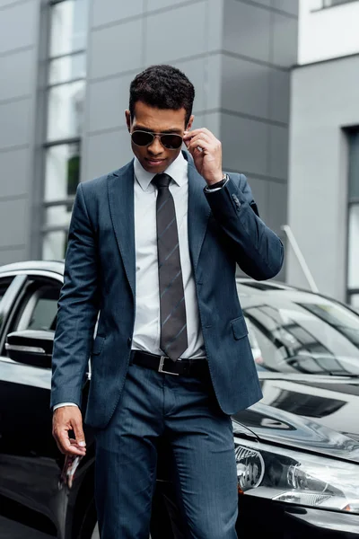 駐車場を歩くスーツとサングラスでハンサムなアフリカ系アメリカ人のビジネスマン — ストック写真